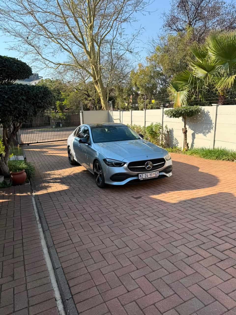 The Mercedes waiting on a brick driveway beside a residential gate