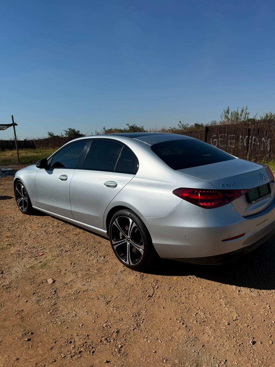 Rear profile of the Mercedes against a blue sky beside a reed fence