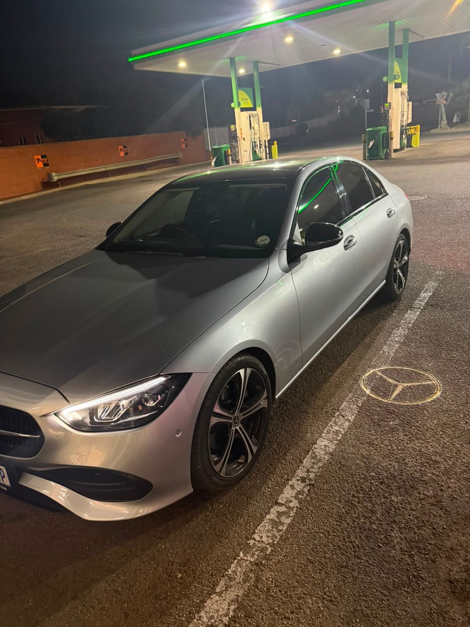 The Mercedes on a filling-station forecourt at night under green canopy light