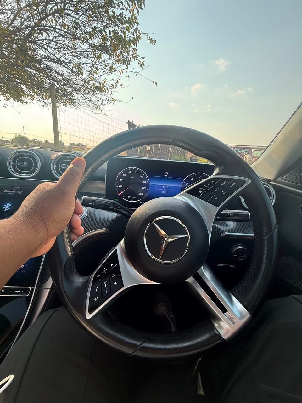 A hand resting on the steering wheel with the instrument cluster lit at dusk